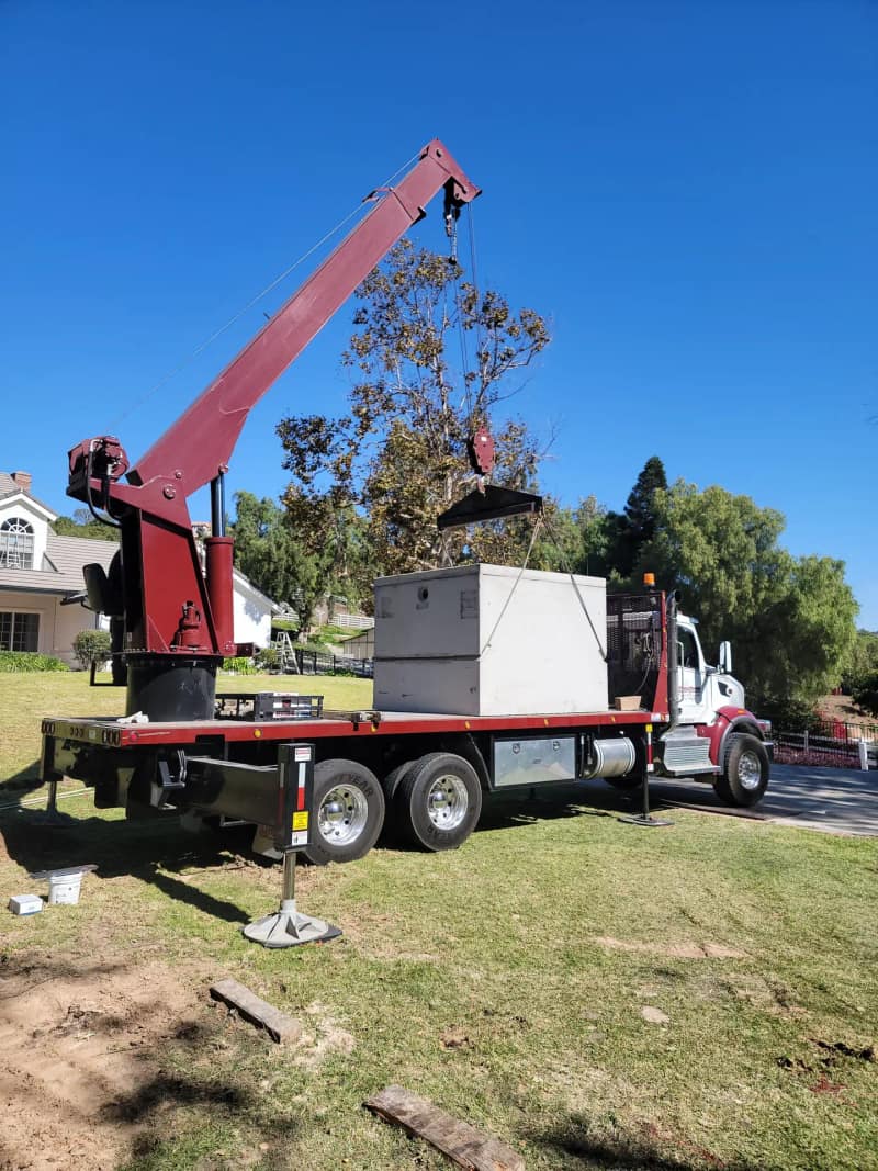 Boom truck with a concrete septic tank rigged on its flatbed, ready to set on a residential lot