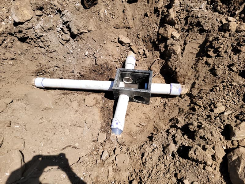 Distribution box and PVC lines in an open trench at the start of a leach field