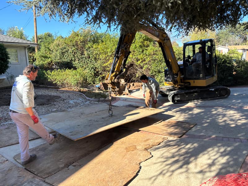 Advanced Sanitation crew guiding a protective ground mat onto a driveway as an excavator lowers it into place