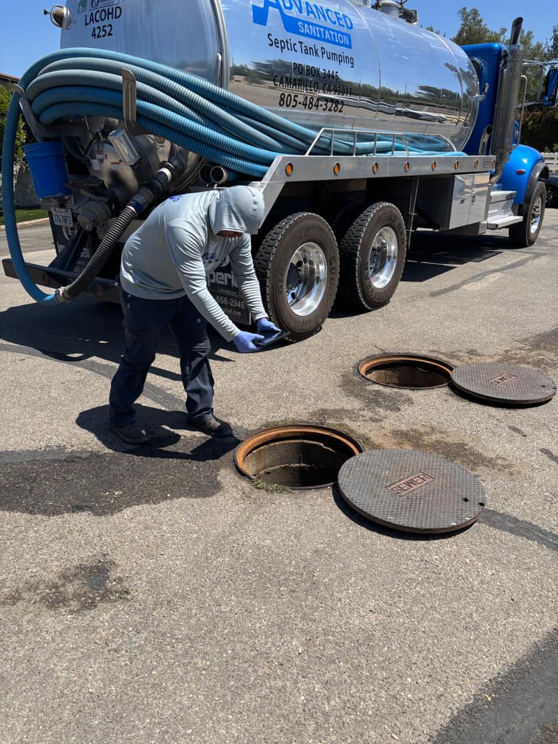Advanced Sanitation technician bending over an open septic tank lid beside the company pump truck