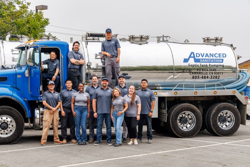 Advanced Sanitation team gathered around a blue company pump truck, with three crew members up on the cab and tank